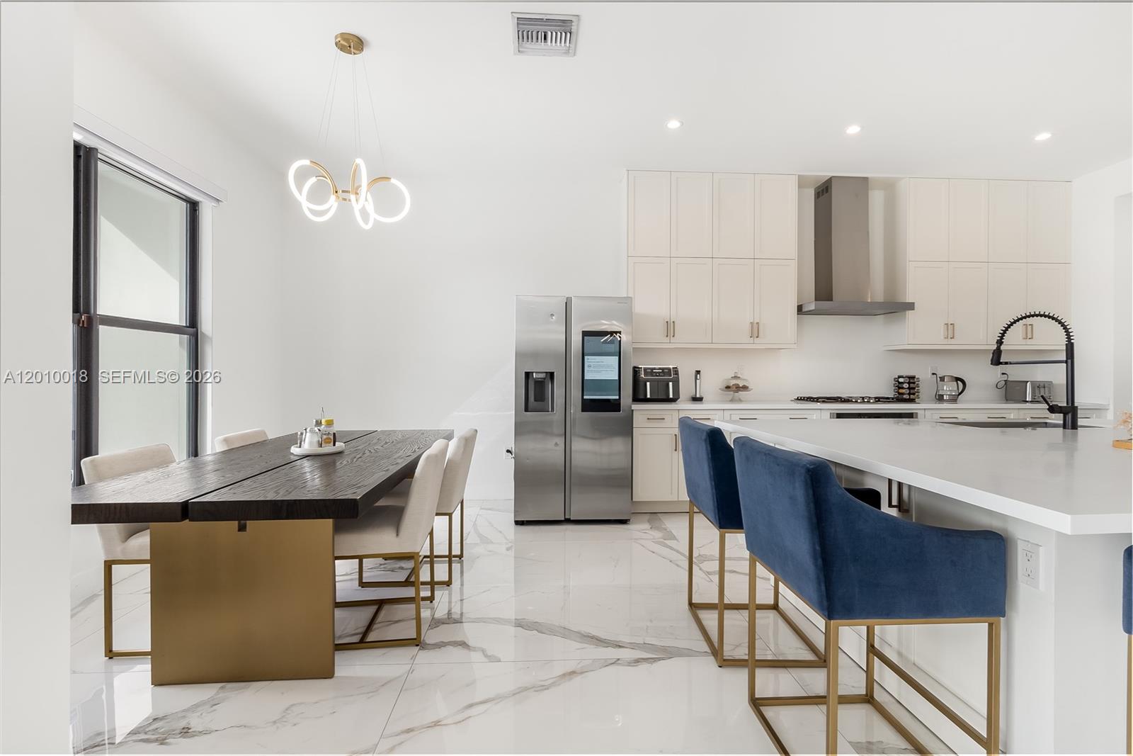 A modern kitchen and dining area features white cabinets, marble floors, and blue bar stools — 17197 Teton River Rd, Boca Raton FL 33496, BOCA RATON, FL