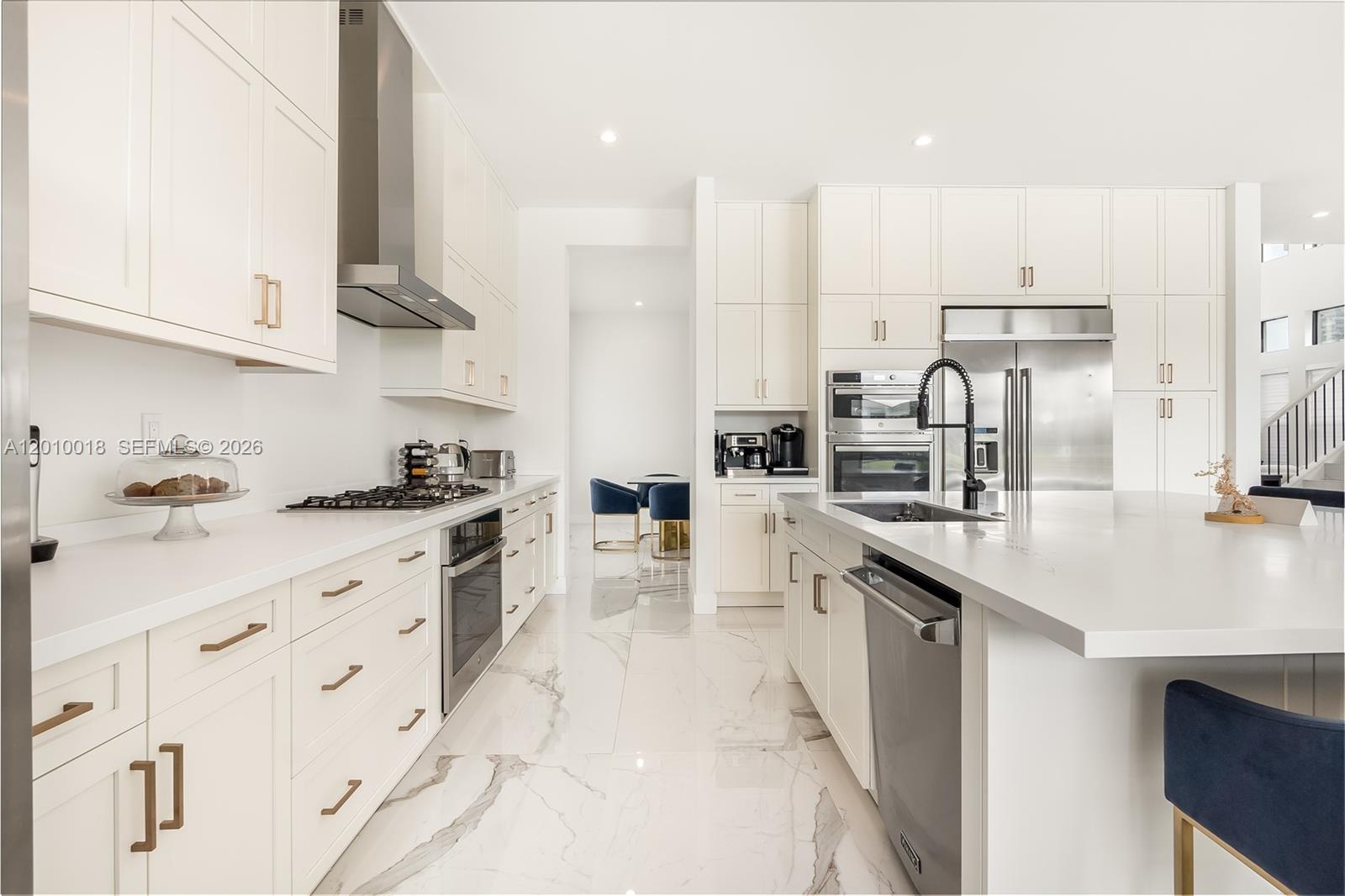 A modern kitchen features white cabinetry, marble-patterned tile floors, stainless steel appliances, and a large island — 17197 Teton River Rd, Boca Raton FL 33496, BOCA RATON, FL