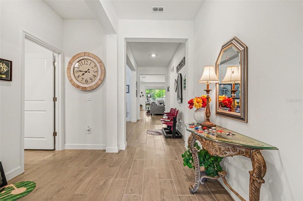 A hallway features light wood-look tile flooring, a large wall clock, and an ornate console table — 10892 IBIS BROOK COURT, LAND O LAKES, FL