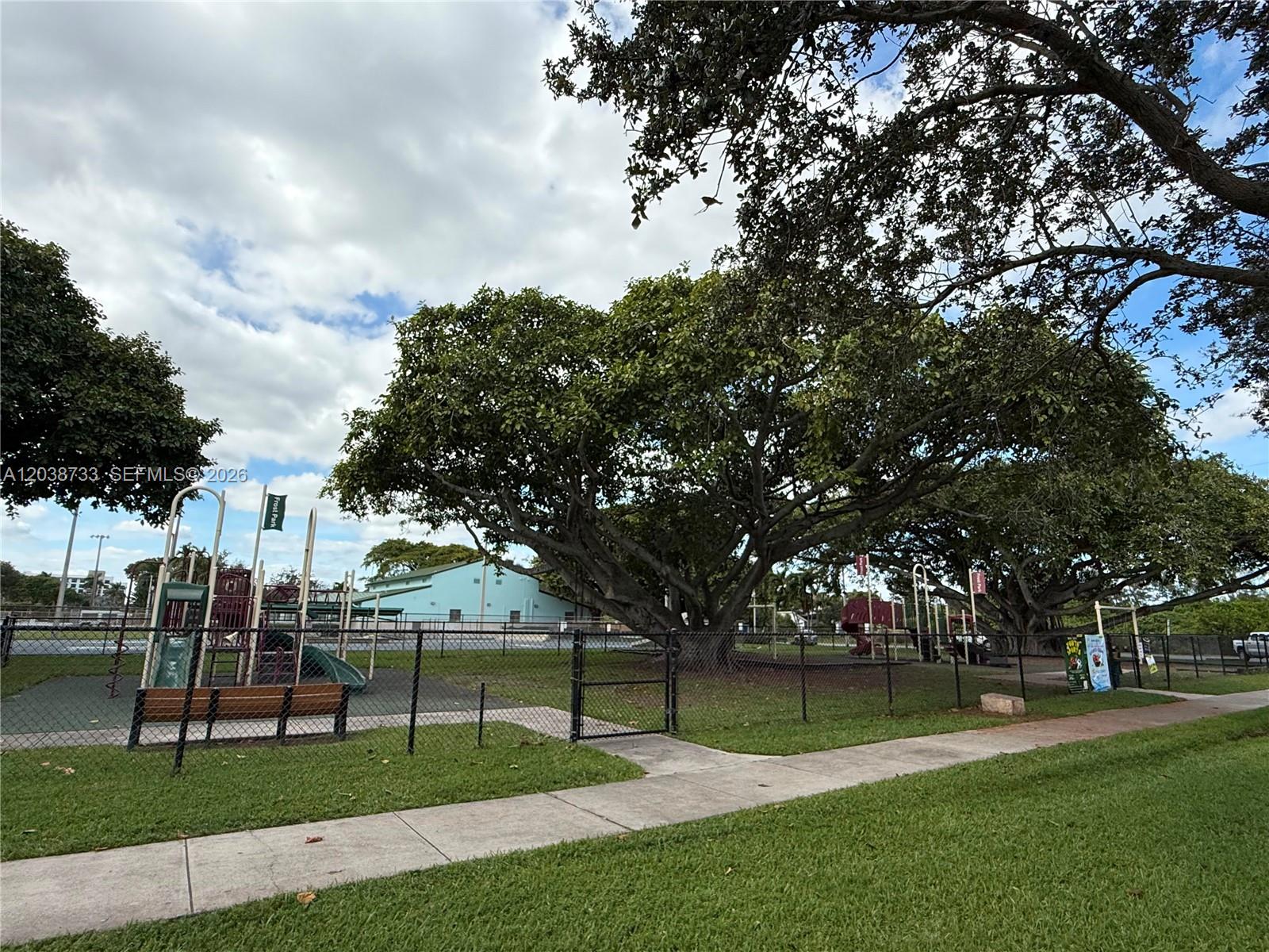 A fenced-in playground features large shade trees, a slide, and a wooden bench — 610 NE 2nd St # 305, Dania Beach FL 33004, DANIA BEACH, FL