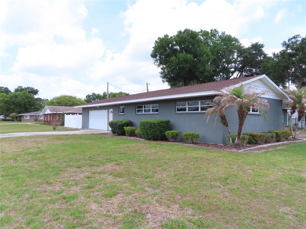 A gray, single-story house with a white garage door and a large front lawn — 5702 JACARANDA AVENUE, LAKELAND, FL