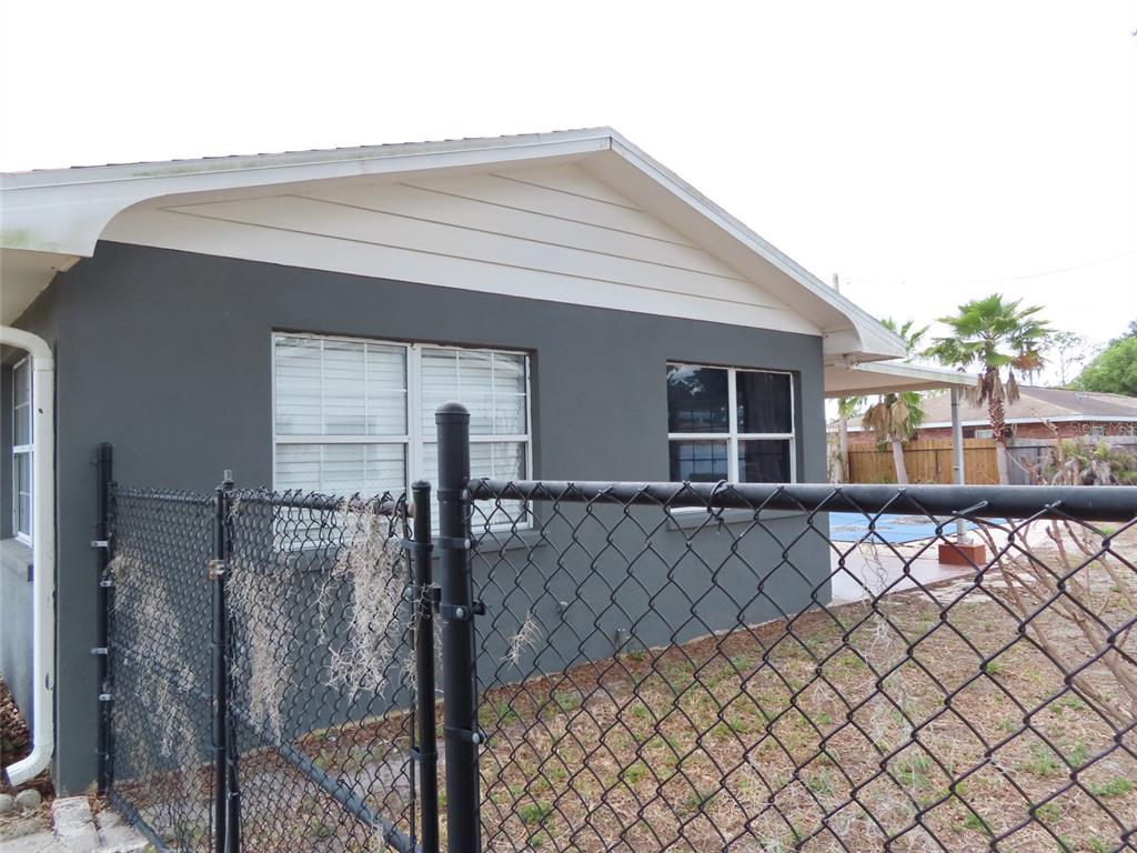 A dark gray exterior wall of a house features two windows behind a chain-link fence — 5702 JACARANDA AVENUE, LAKELAND, FL
