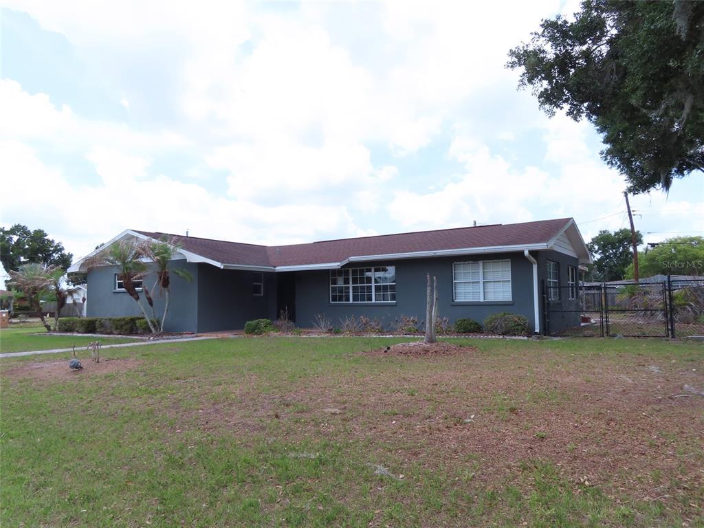 A single-story gray house with a brown shingled roof sits on a grassy lot — 5702 JACARANDA AVENUE, LAKELAND, FL