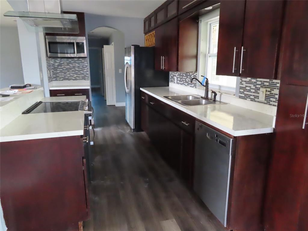 A kitchen features dark wood cabinets, white countertops, stainless steel appliances, and a tiled backsplash — 5702 JACARANDA AVENUE, LAKELAND, FL
