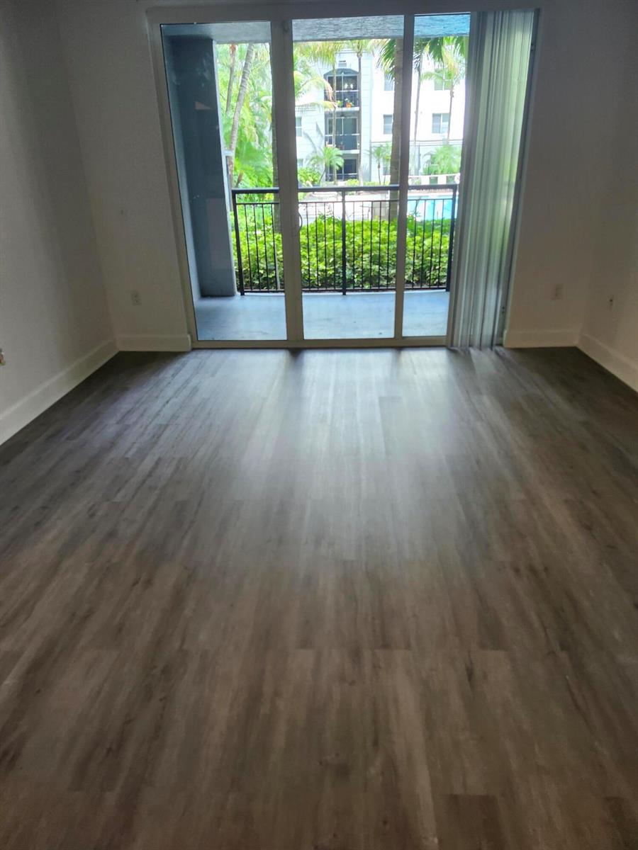 An empty room with wood-look flooring and a sliding glass door leading to a balcony — 1660 Renaissance Commons Boulevard # 2122, Boynton Beach FL 33426, BOYNTON BEACH, FL