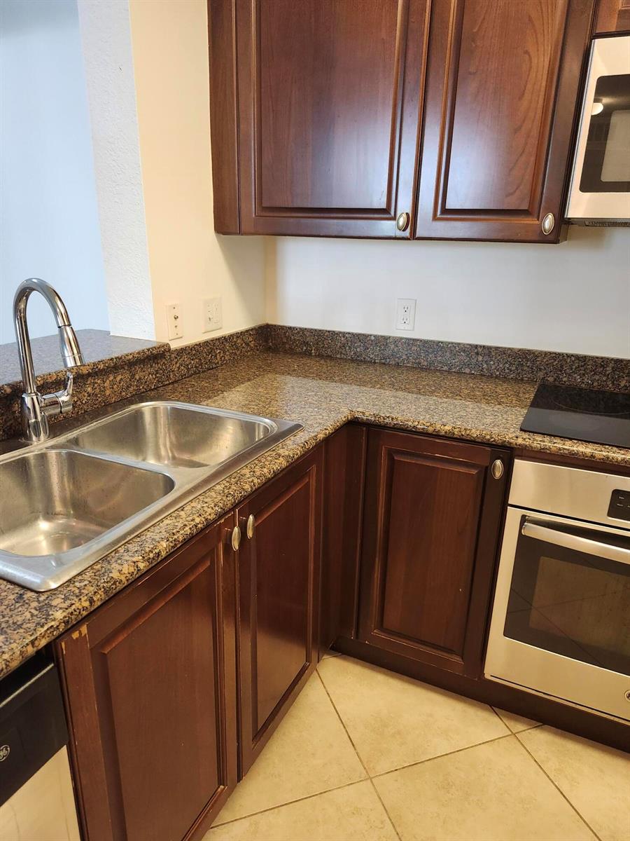 A kitchen features dark wood cabinets, granite countertops, a stainless steel sink, and stainless appliances — 1660 Renaissance Commons Boulevard # 2122, Boynton Beach FL 33426, BOYNTON BEACH, FL