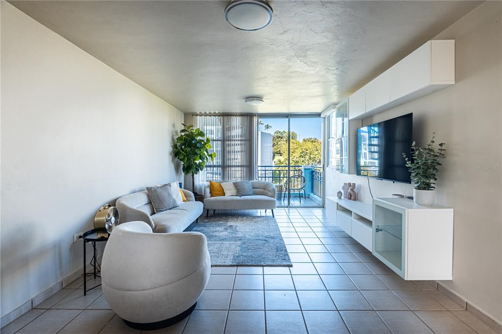 A living room features light tile floors, a white sofa, and a wall-mounted television unit — Apto 14-402 COSTA BRAVA, CEIBA, PR