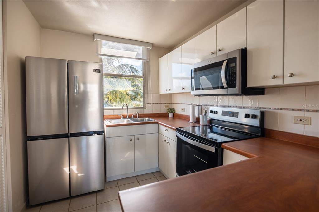 A kitchen features stainless steel appliances, white cabinets, and wood-toned countertops — Apto 14-402 COSTA BRAVA, CEIBA, PR