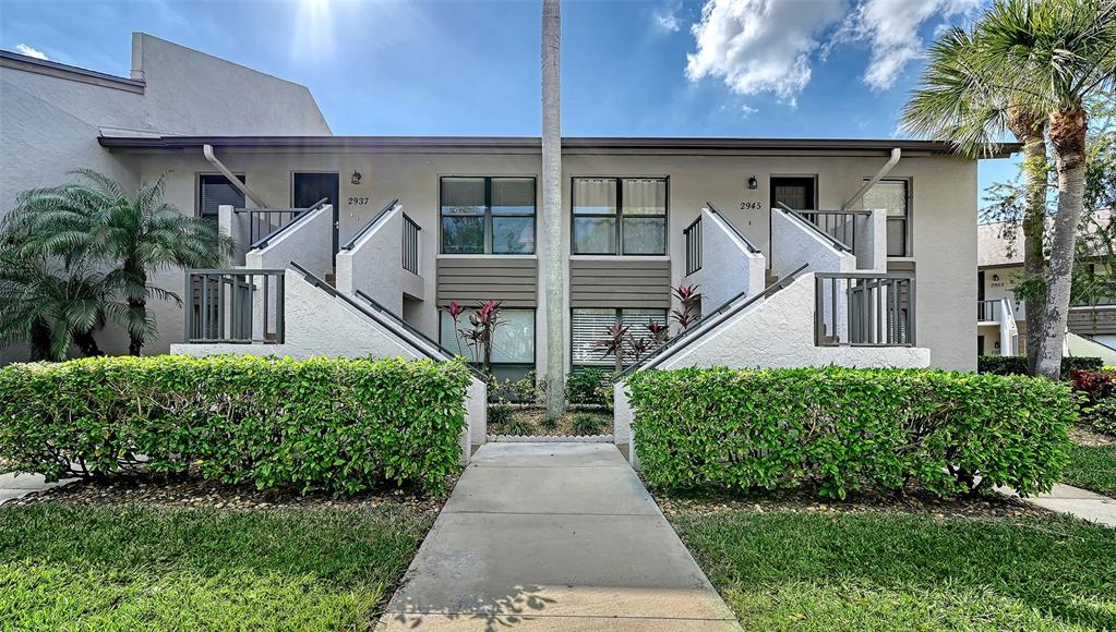 A two-story apartment building exterior features a central walkway, stairs, and manicured hedges — 2937 TAYWOOD MEADOWS UNIT 32, SARASOTA, FL