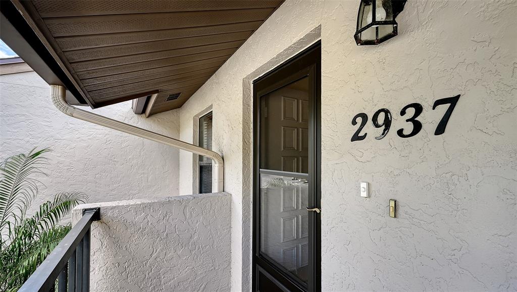 The exterior entrance features a white stucco wall, a dark storm door, and a downspout — 2937 TAYWOOD MEADOWS UNIT 32, SARASOTA, FL