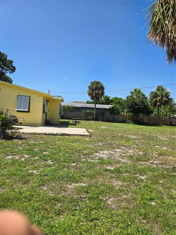 A yellow house with a concrete patio sits in a large, grassy backyard with palm trees — 239 NE 18TH AVENUE, POMPANO BEACH, FL