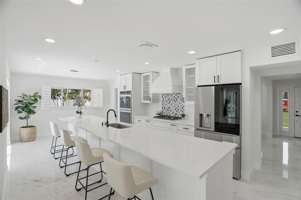 A modern white kitchen features a long island with bar seating and stainless steel appliances — 5101 DOVER STREET NE, ST PETERSBURG, FL