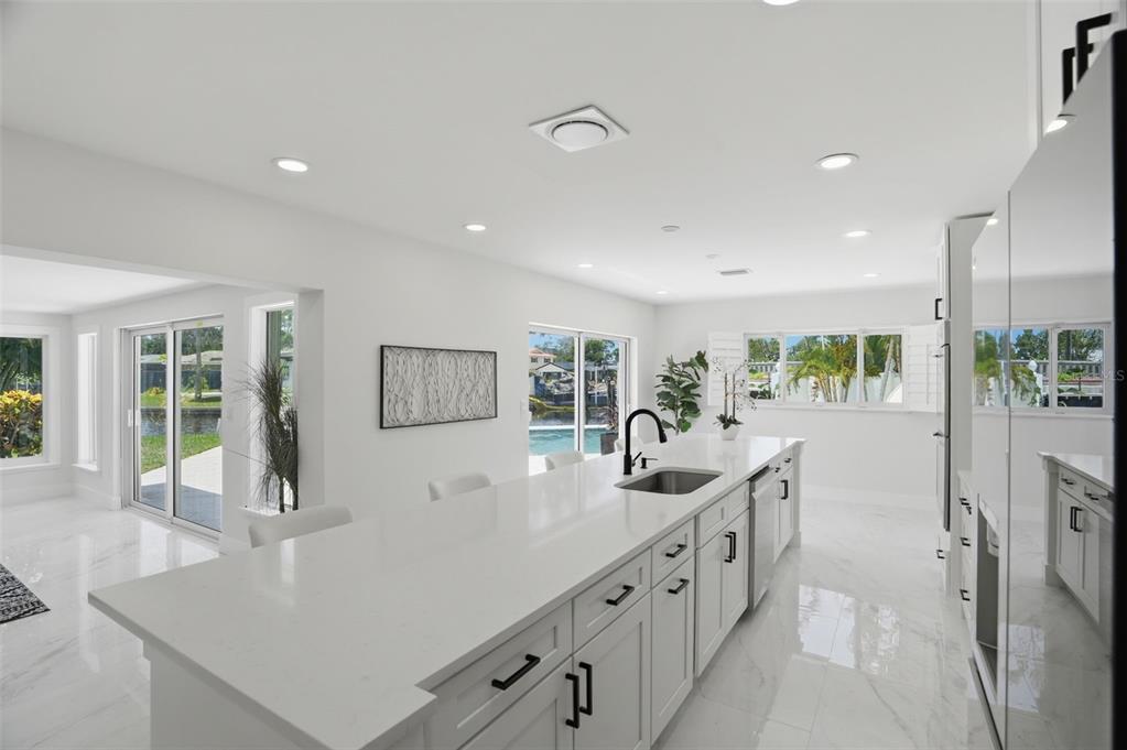 A modern white kitchen features a large island with a sink and marble-look tile flooring — 5101 DOVER STREET NE, ST PETERSBURG, FL