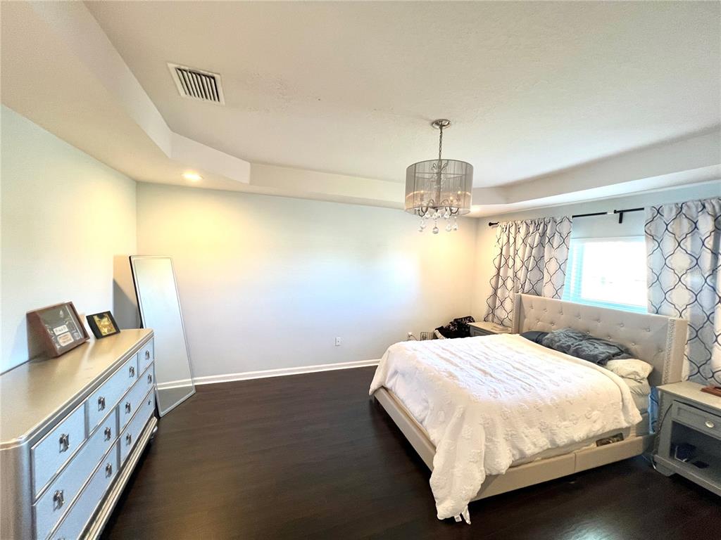 A bedroom features dark wood flooring, a tufted headboard bed, and a silver chandelier — 4639 POND RIDGE DRIVE, RIVERVIEW, FL