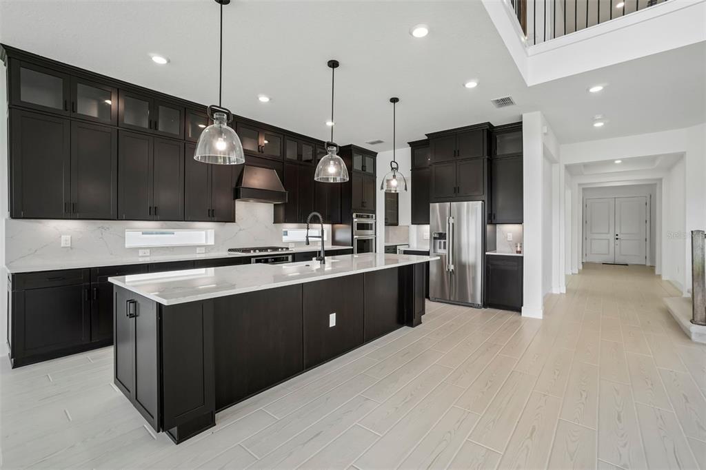 A modern kitchen features dark cabinetry, a large white quartz island, and light wood flooring — 6719 ASBURY BARNES LANE, WESLEY CHAPEL, FL