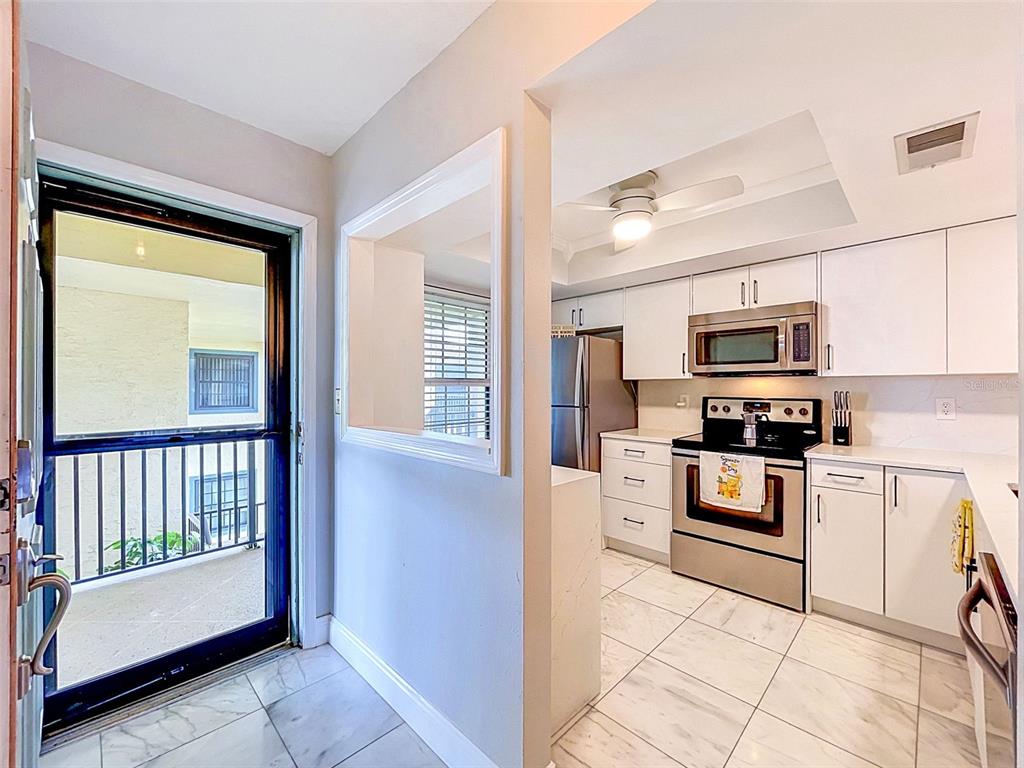 A view from an entryway into a white kitchen with stainless steel appliances and tile flooring — 460 S PAULA DR UNIT 107, DUNEDIN, FL
