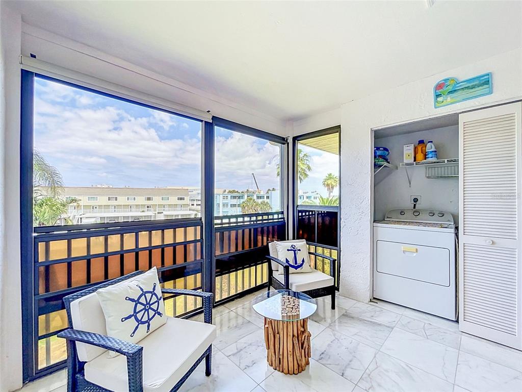 A sunroom features tile flooring, two chairs with anchor pillows, and an in-unit laundry closet — 460 S PAULA DR UNIT 107, DUNEDIN, FL