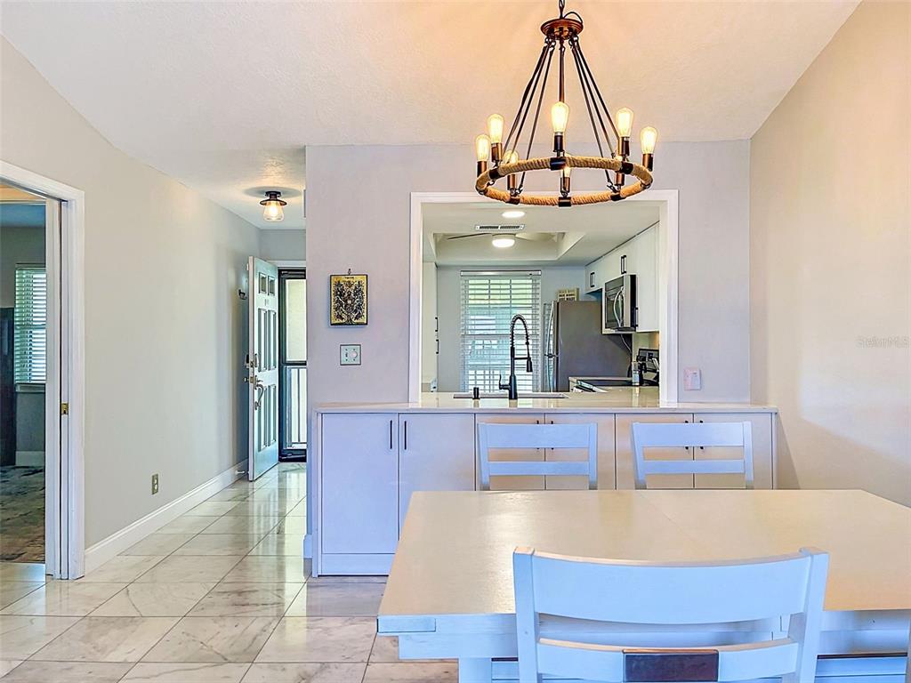 A dining area features a rope chandelier, white cabinetry, and a view into the kitchen — 460 S PAULA DR UNIT 107, DUNEDIN, FL