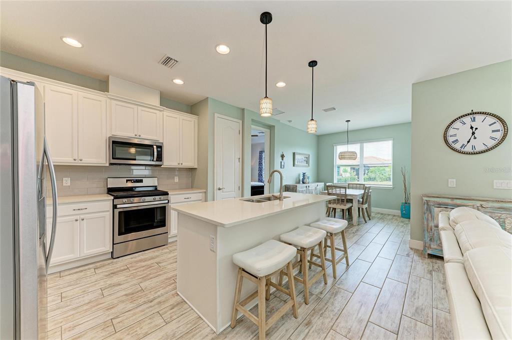 A kitchen with white cabinets, a central island with stools, and light wood-look tile flooring — 4809 TOBERMORY WAY, BRADENTON, FL