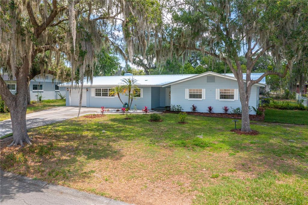A light blue single-story house with a metal roof sits behind large moss-draped trees — 2230 W HELEN CIRCLE, BARTOW, FL