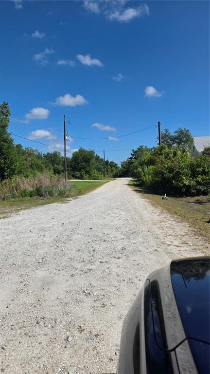A gravel road stretches forward between utility poles and dense green vegetation under a blue sky — 2094 MIDDLE TERRACE, PUNTA GORDA, FL