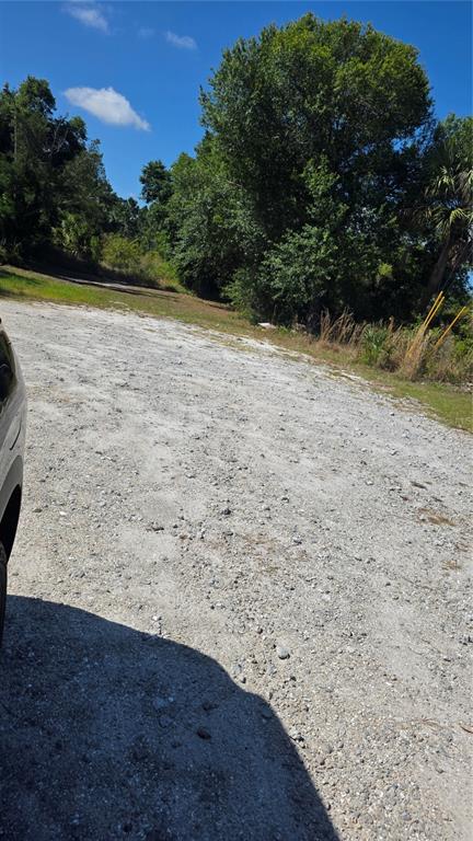 A gravel driveway leads toward a wooded area under a clear blue sky — 2094 MIDDLE TERRACE, PUNTA GORDA, FL