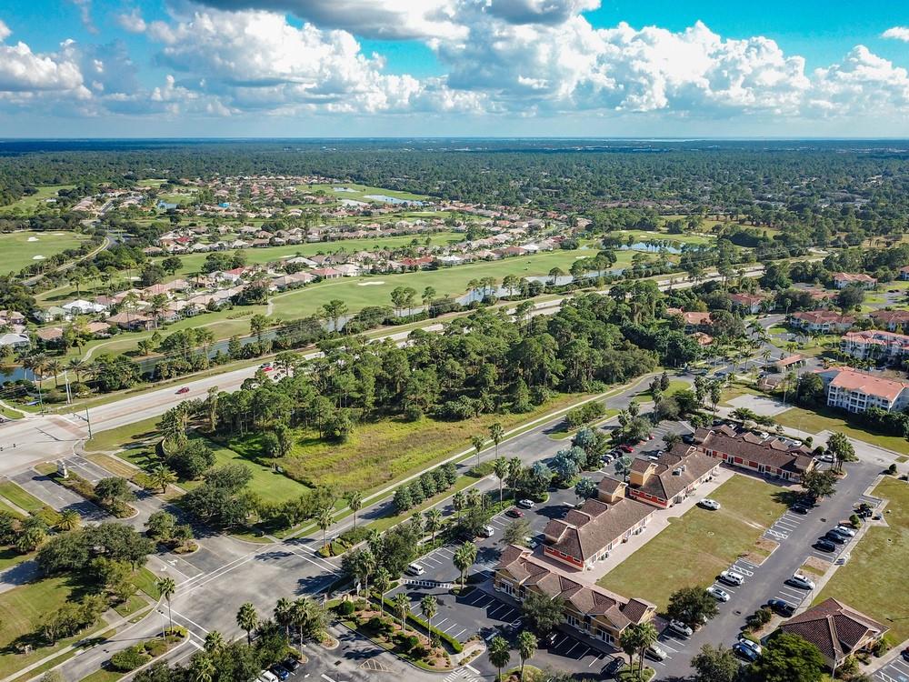 An aerial view shows a commercial plaza with parking lots adjacent to a residential golf course — 3020 BOBCAT VILLAGE CENTER ROAD, NORTH PORT, FL