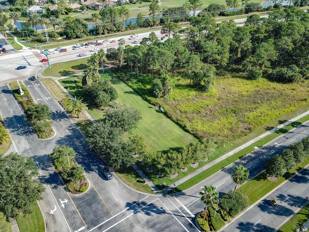 An aerial view shows a vacant, grassy lot situated between two paved roads and trees — 3020 BOBCAT VILLAGE CENTER ROAD, NORTH PORT, FL