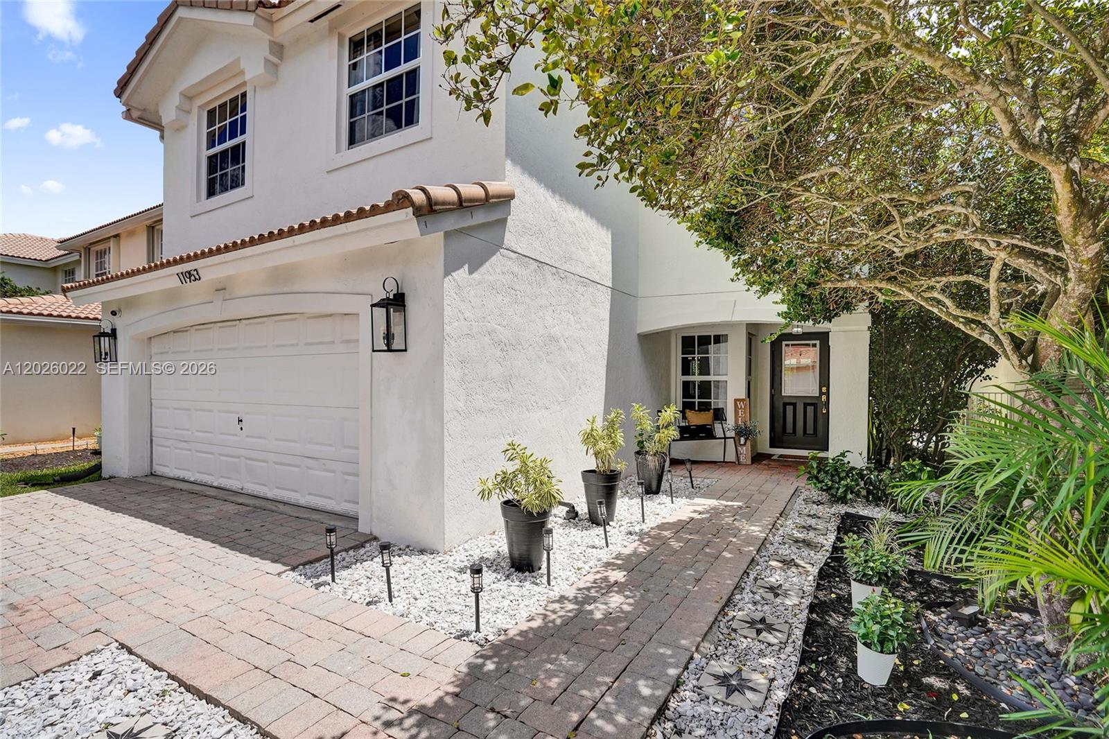 A two-story white stucco house features a garage, a brick walkway, and potted plants — 11953 Donlin Dr, Wellington FL 33414, WELLINGTON, FL