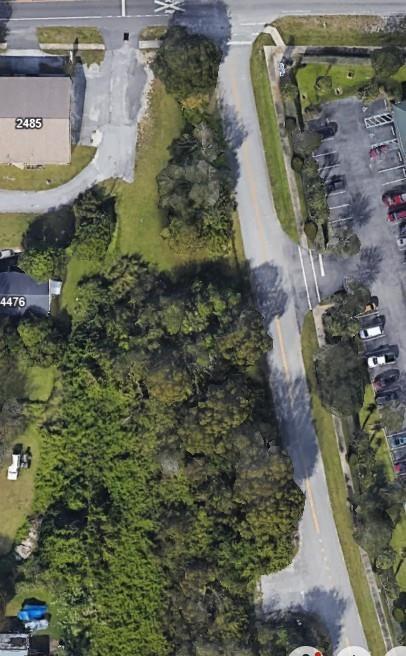 An aerial view shows a wooded lot situated between a paved road and buildings — 4465 24th Avenue, Vero Beach FL 32967, VERO BEACH, FL
