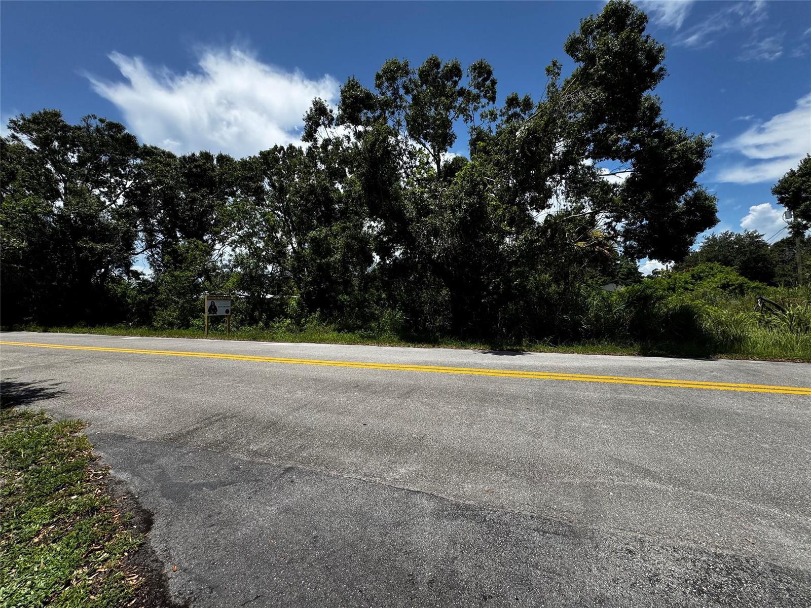 A paved road runs in front of a wooded lot with a for-sale sign — 4465 24th Avenue, Vero Beach FL 32967, VERO BEACH, FL
