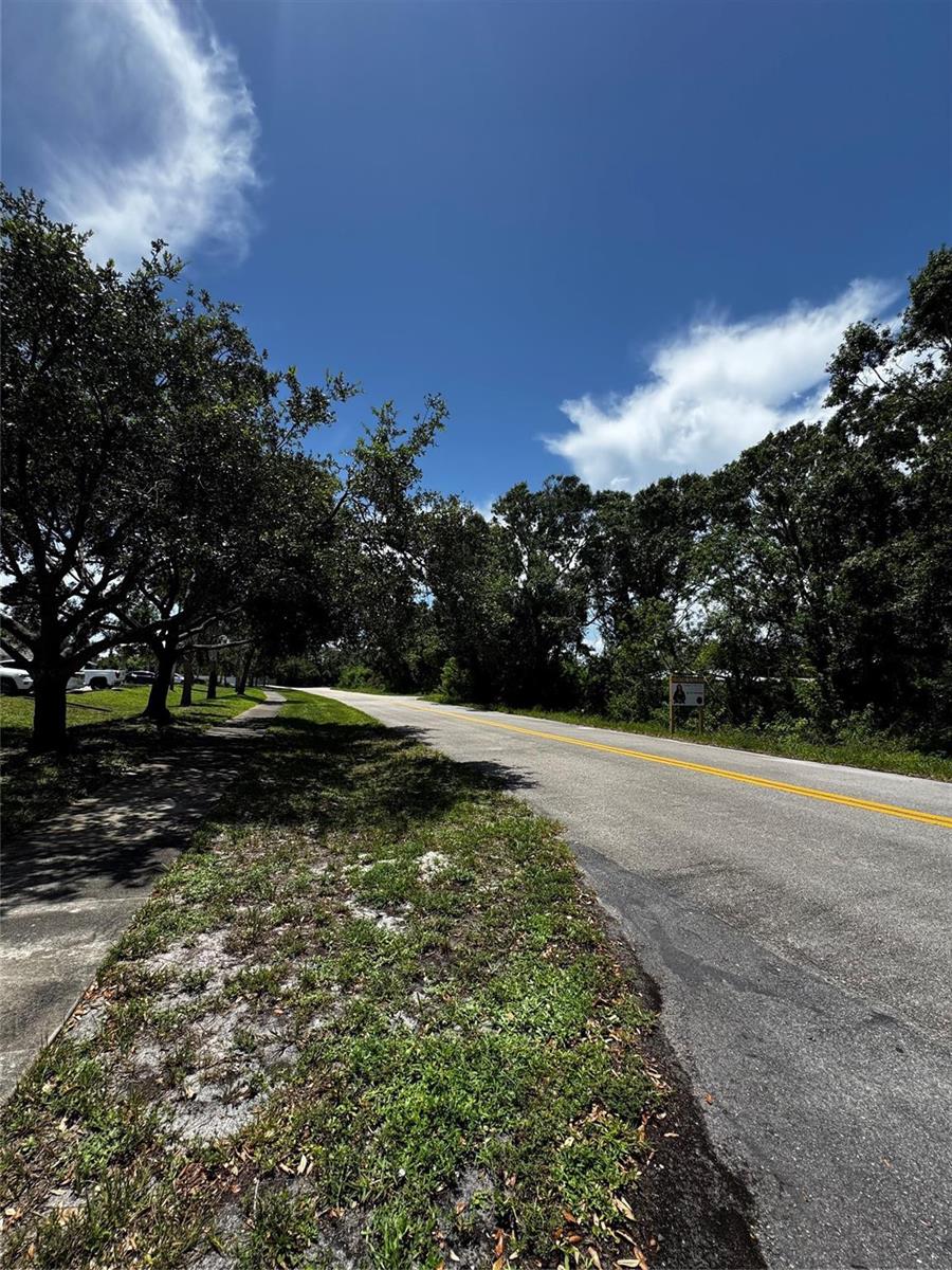 A paved road with a yellow center line runs alongside a grassy area and trees — 4465 24th Avenue, Vero Beach FL 32967, VERO BEACH, FL