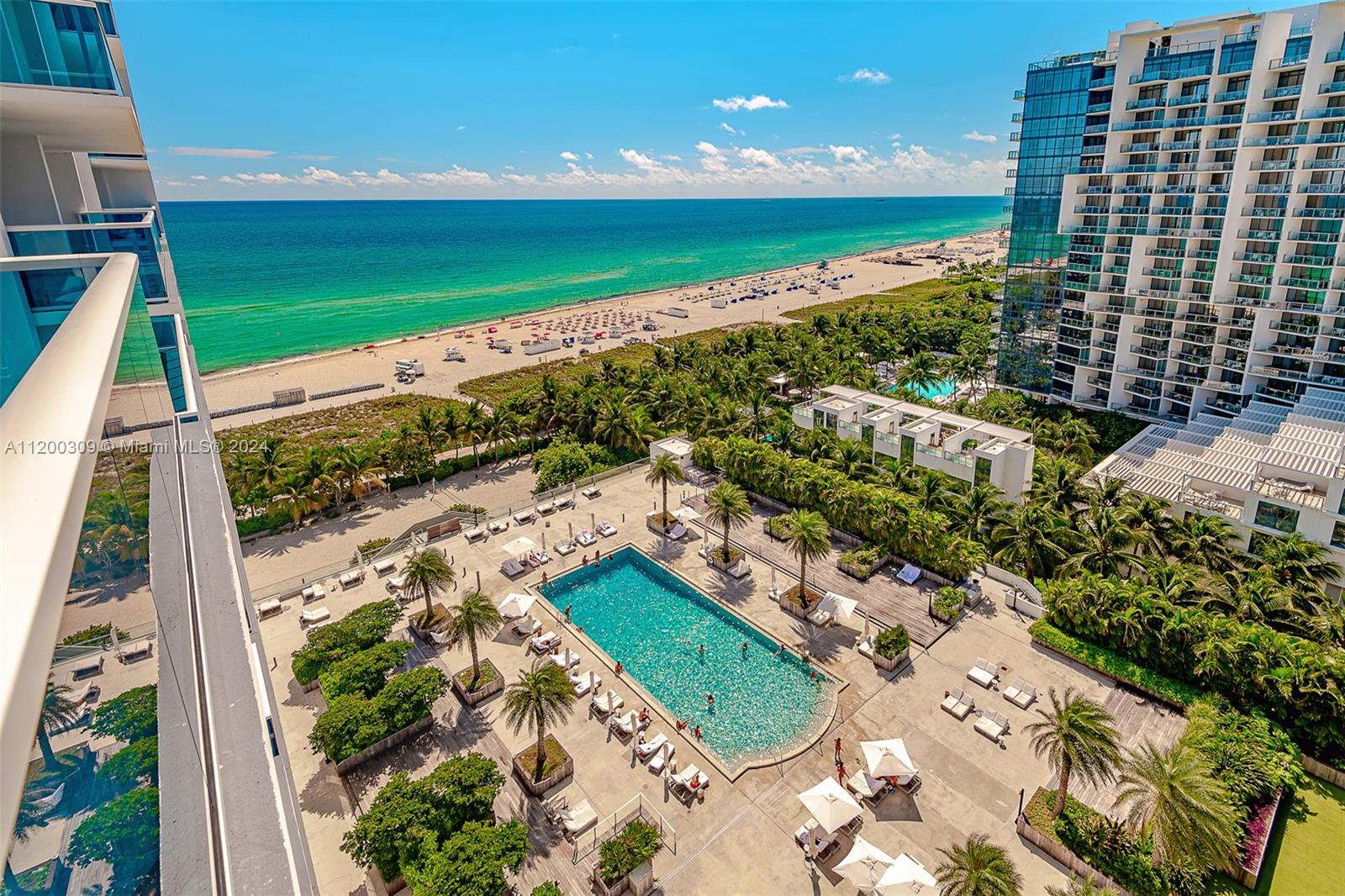 An elevated view shows a swimming pool deck surrounded by palm trees near a beach — 2301 Collins Ave # 1506, Miami Beach FL 33139, MIAMI BEACH, FL