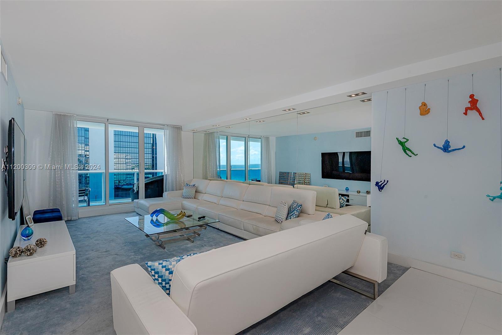 A living room features a white sectional sofa, glass coffee table, and wall-mounted climbing figures — 2301 Collins Ave # 1506, Miami Beach FL 33139, MIAMI BEACH, FL