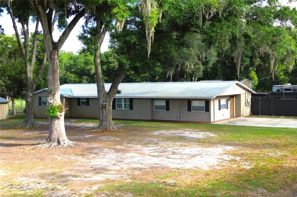 A single-story house with a metal roof and tan siding sits on a wooded lot — 5009 VAUGHN ROAD, PLANT CITY, FL