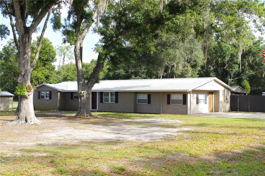 A single-story house with a metal roof and brick siding sits among large oak trees — 5009 VAUGHN ROAD, PLANT CITY, FL