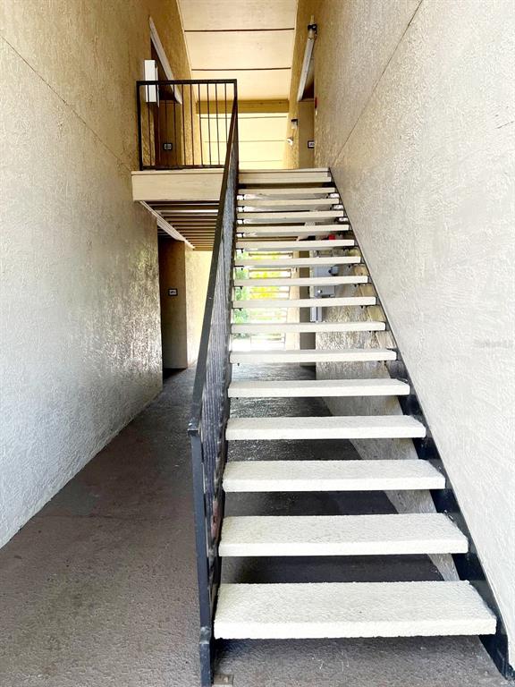 An outdoor staircase with metal railings leads to an upper-level walkway between two stucco walls — 4069 CROCKERS LAKE BOULEVARD UNIT 24, SARASOTA, FL