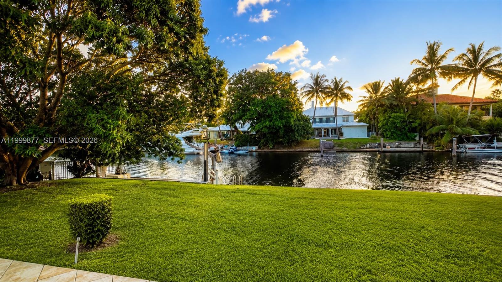A grassy backyard overlooks a canal with docked boats and a house across the water — 4403 Palm Ln, Miami FL 33137, MIAMI, FL