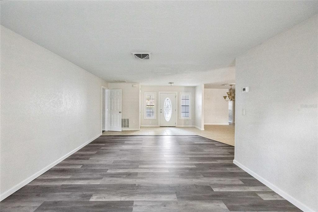 A living room with grey wood-look flooring, white walls, and a front entry door — 4369 MARINE PARKWAY, NEW PORT RICHEY, FL