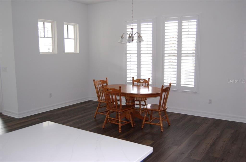 A dining area features a wooden table with four chairs, white walls, and dark flooring — 1827 BEACH RIDGE ROAD, CELEBRATION, FL