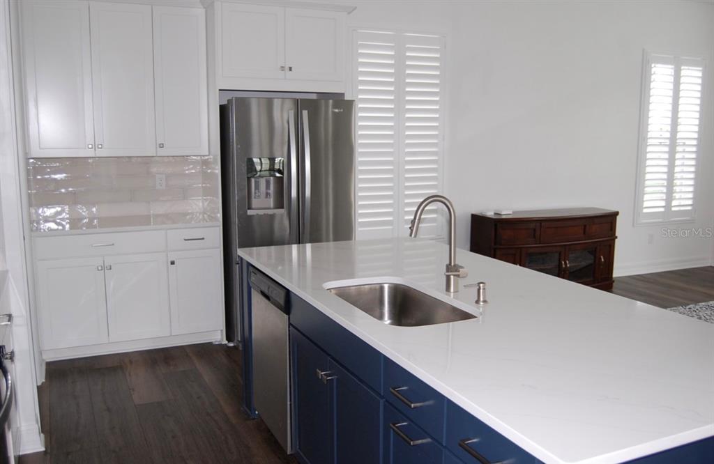 A kitchen features white upper cabinets, a blue island with a sink, and stainless steel appliances — 1827 BEACH RIDGE ROAD, CELEBRATION, FL