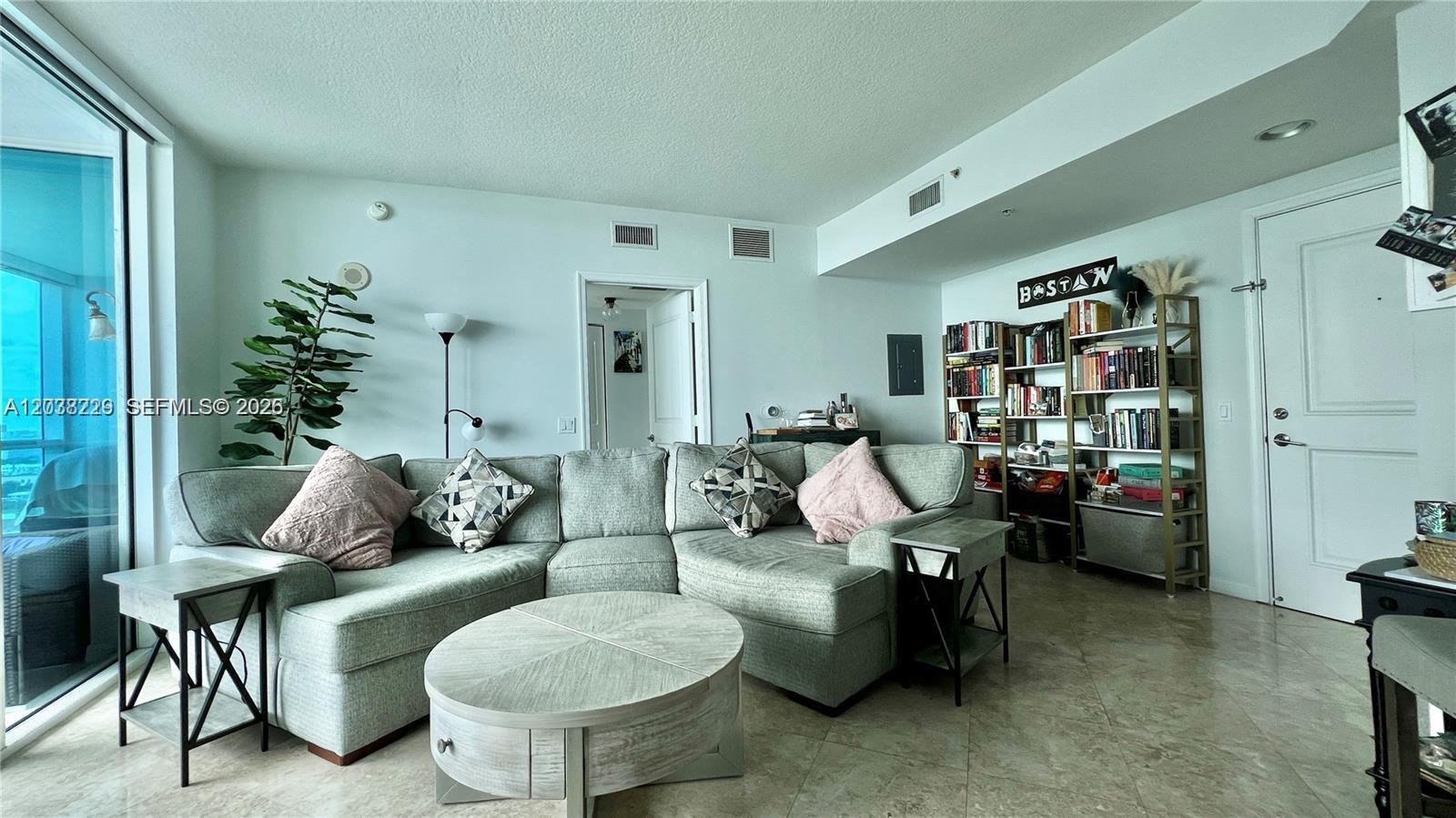 A living room features a sectional sofa, a round coffee table, and tall bookshelves — 480 NE 30th St # 1603, Miami FL 33137, MIAMI, FL