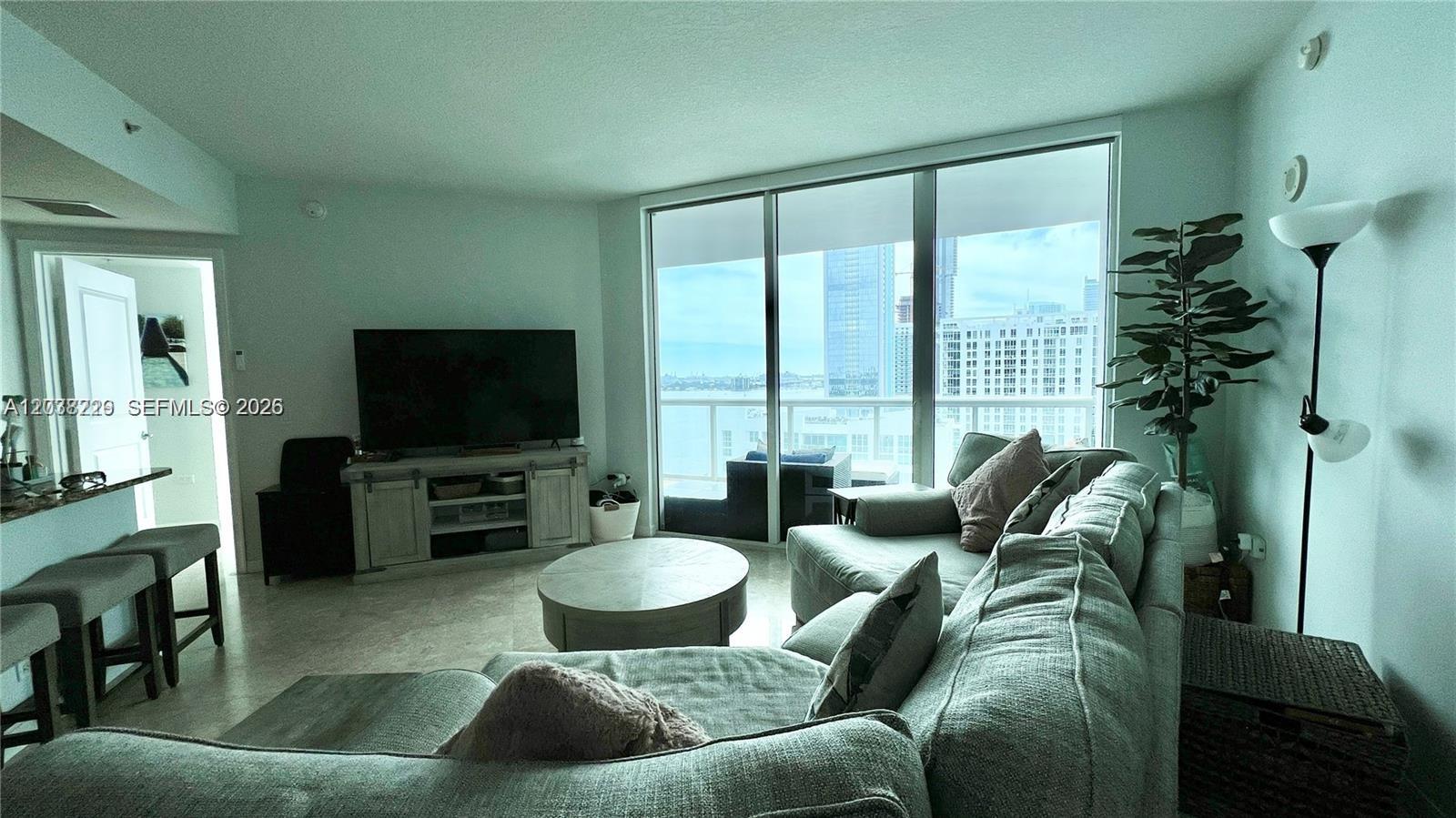A living room features a sectional sofa, a round coffee table, and floor-to-ceiling windows — 480 NE 30th St # 1603, Miami FL 33137, MIAMI, FL