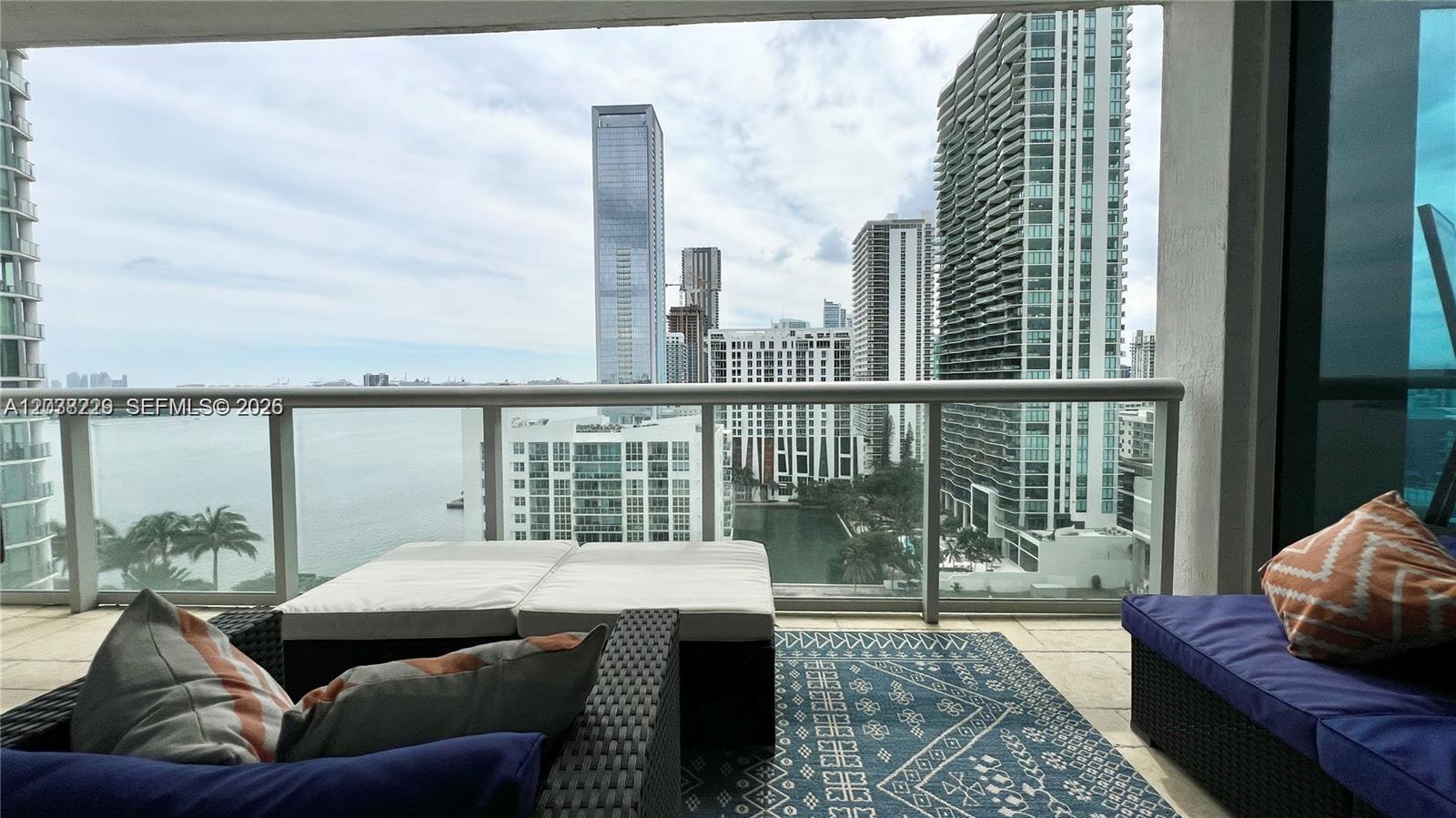 A balcony with outdoor furniture overlooks a bay and a city skyline — 480 NE 30th St # 1603, Miami FL 33137, MIAMI, FL