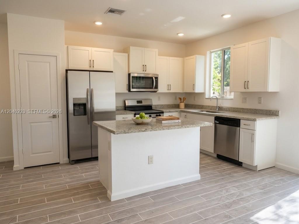 A kitchen features white cabinets, stainless steel appliances, a granite island, and wood-look tile flooring — 1019 SE 24th Ter, Homestead FL 33035, HOMESTEAD, FL