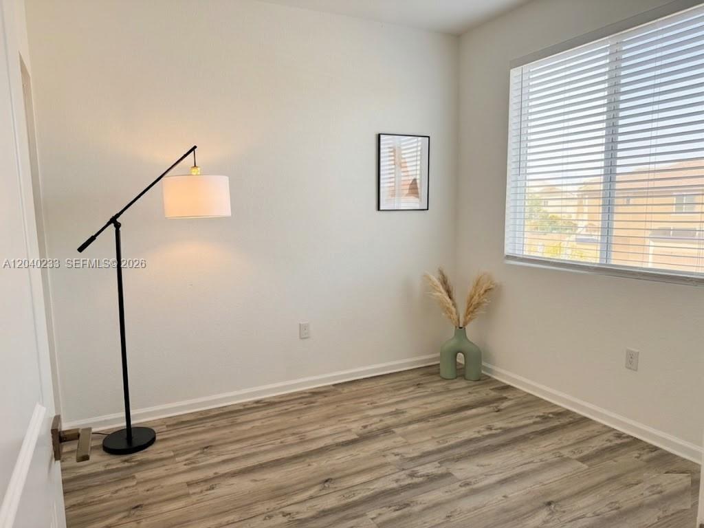 An empty room features wood-look flooring, a floor lamp, a small wall picture, and a window — 1019 SE 24th Ter, Homestead FL 33035, HOMESTEAD, FL