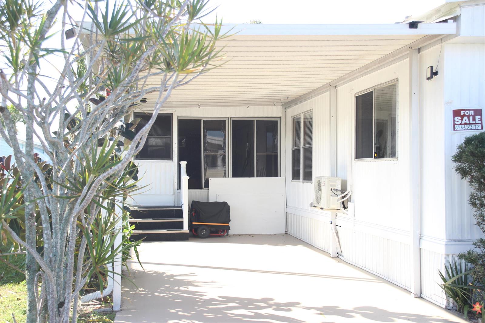 A white mobile home exterior features a covered carport, a small staircase, and a for-sale sign — 58009 Bahama Bay, Boynton Beach FL 33436, BOYNTON BEACH, FL