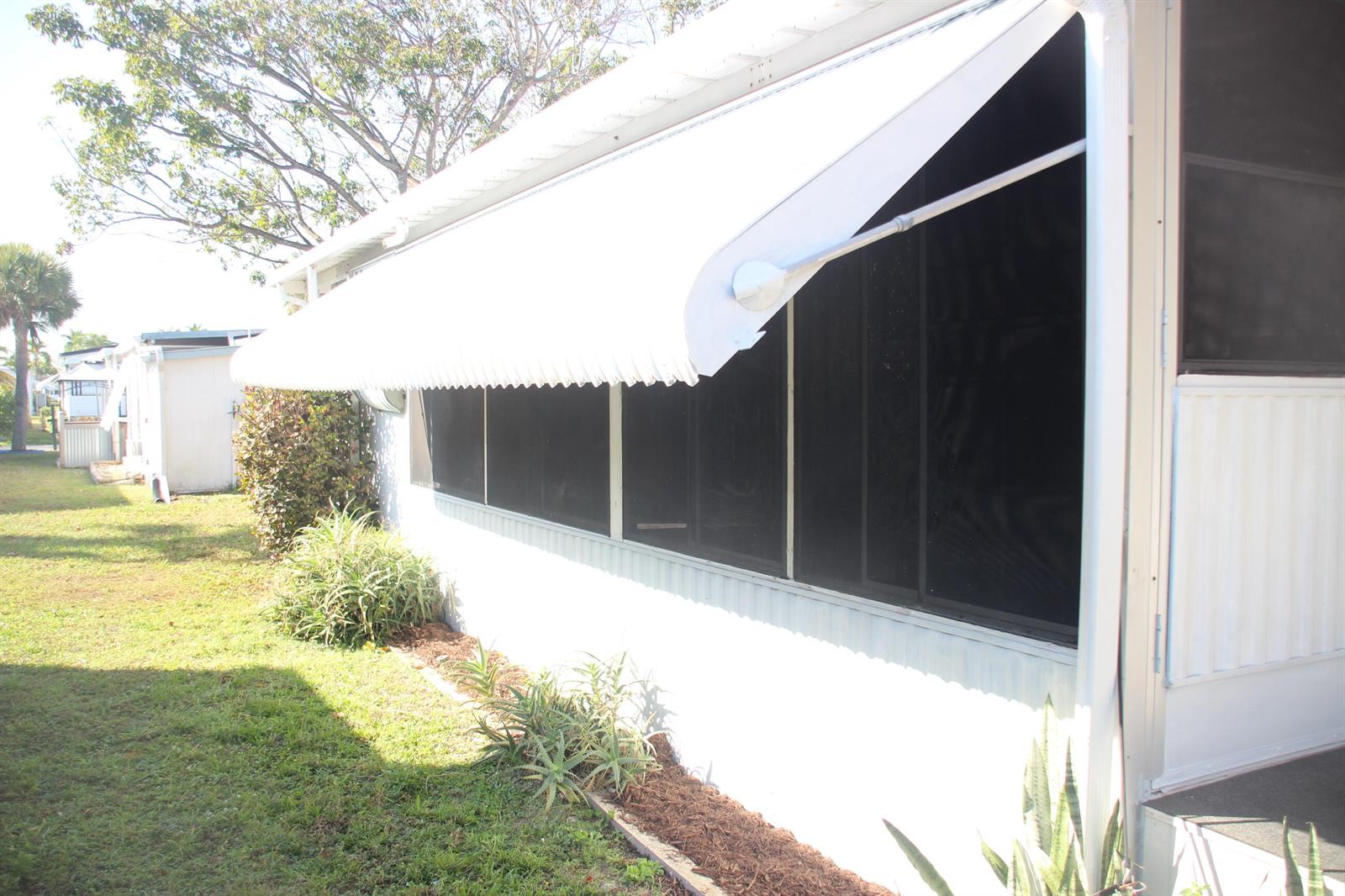 The exterior of a mobile home features a white metal awning over screened-in windows — 58009 Bahama Bay, Boynton Beach FL 33436, BOYNTON BEACH, FL