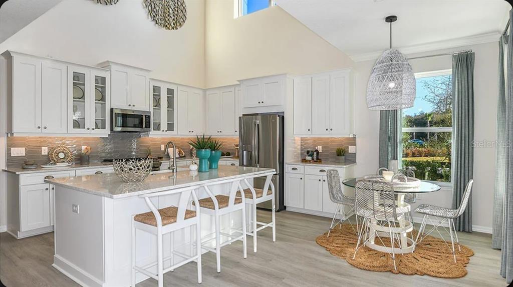 A bright kitchen features white cabinetry, a large island with bar stools, and dining area — 5168 DOMINION ALLEY, ST CLOUD, FL