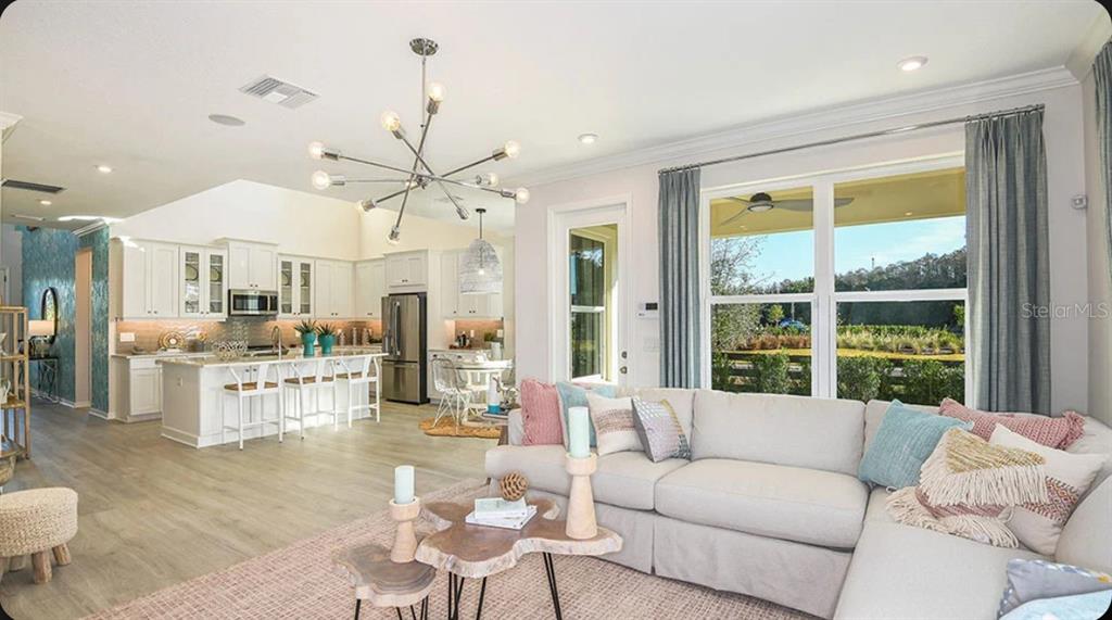 An open-concept living room and kitchen featuring a sectional sofa, chandelier, and large windows — 5168 DOMINION ALLEY, ST CLOUD, FL
